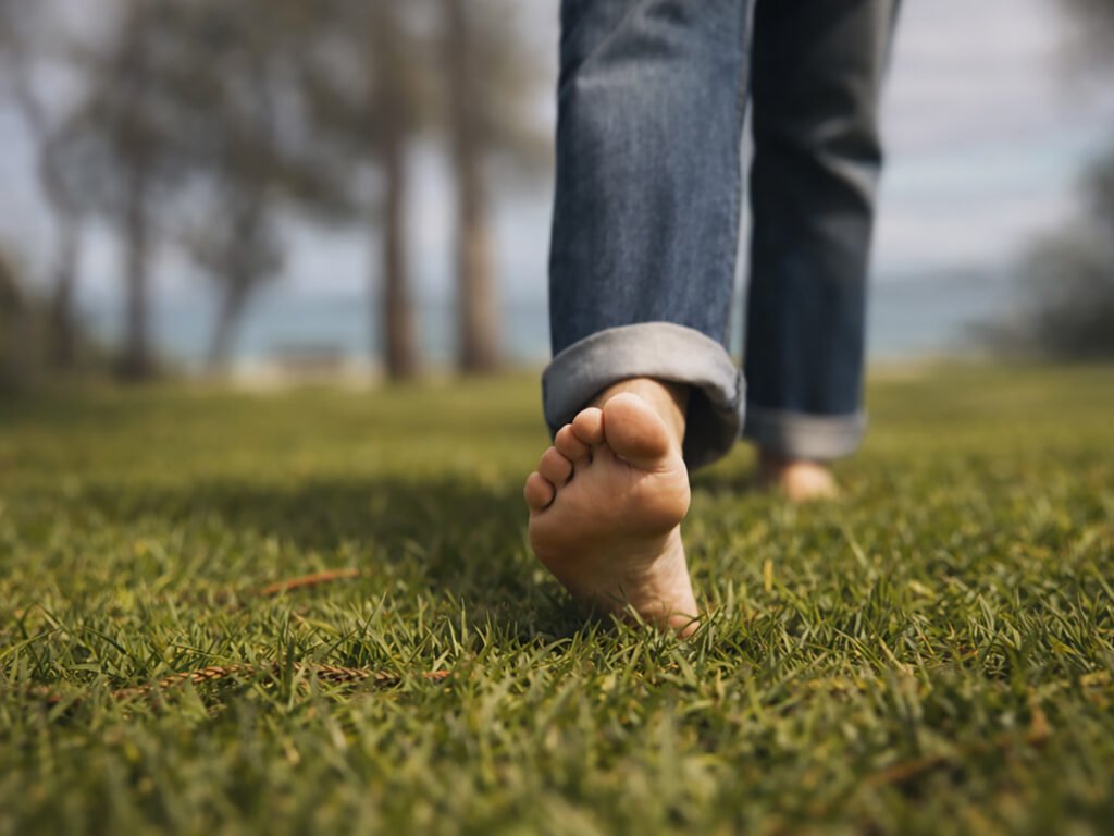 Barefoot sole stepping onto grass, with ocean and trees softly blurred in the background